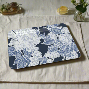 A decorative tray with delicate white peony illustrations over a navy blue background, resting on a textured linen table setting.