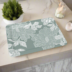 A muted sage-green tray with an intricate white floral design, styled on a marble countertop with candles.