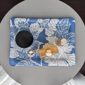 A decorative tray with intricate white floral patterns, neatly holding skincare and perfume bottles on a vanity table.