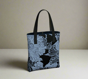 A tote bag with light blue and black floral print, with black vegan leather straps.