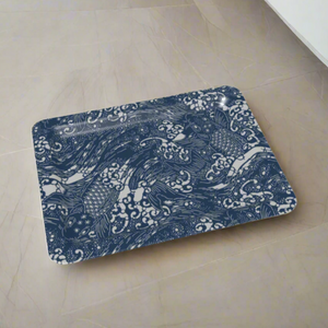 Rectangular tray with rounded corners, decorated with blue and white koi fish swimming through stylized waves, shown resting on a pale stone tile floor