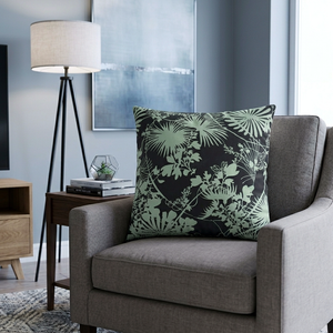 Gray armchair with a decorative pillow featuring green leaf patterns in a living room setting.