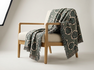 Wooden armchair with a patterned green blanket draped over it on a plain background