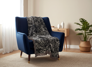 Woven blanket featuring a dark blue and off-white katagami pattern of stylized koi fish swimming through swirling waves and water currents, with a fringed edge, draped over a blue armchair.