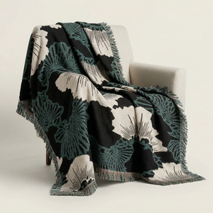 Woven blanket featuring a stylized Japanese pine motif in black, ecru, and dark teal, draped over an armchair.