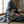 Woven blanket with a dark blue and off-white katagami-inspired pattern featuring stylized chrysanthemums, leaves, and stripes. The blanket has a multicolored fringe and is draped over a person sitting on a tatami mat.