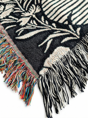Corner edge of a woven blanket featuring a dynamic, abstract pattern of stylized mist in off-white against a black background. 
