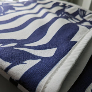 Microfiber and cotton terry towel hanging against a tiled wall, showcasing a dark blue and white ‘Trellis’ pattern. Hemmed edges add durability.