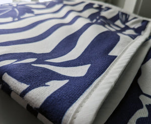 Microfiber and cotton terry towel hanging against a tiled wall, showcasing a dark blue and white ‘Trellis’ pattern. Hemmed edges add durability.