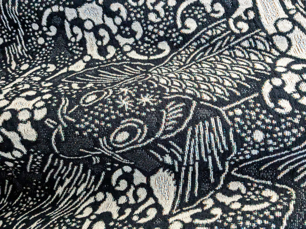 Close-up of a woven blanket featuring a dark blue and white pattern of stylized koi fish. 