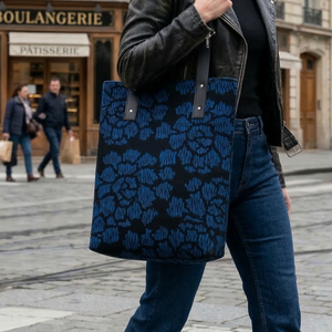 Black tote bag with a repeating blue stylized peony pattern, featuring fine, striated details within the blossoms, on a black background. The bag has black leather straps.