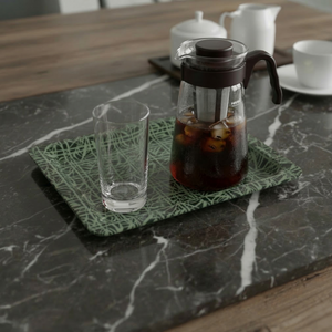 Glass carafe with iced coffee on a green tray on a marble surface