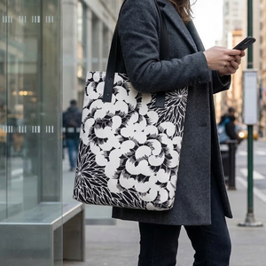 White and black tote bag with a pattern of large, swirling, stylized floral forms on the main body, complemented by a contrasting motif of fine, radiating lines resembling abstract leaves or starbursts.