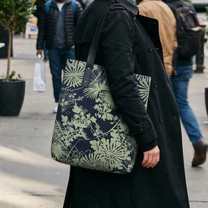 Dark blue tote bag with a light olive green botanical pattern featuring stylized fan-like leaves and intertwining vines.