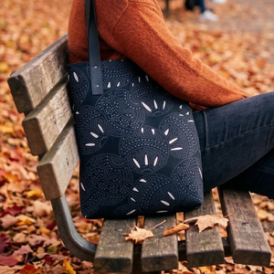 Dark grey tote bag featuring a pattern of abstract circular motifs with intricate light grey dotted infill, accented by white petal-like shapes.