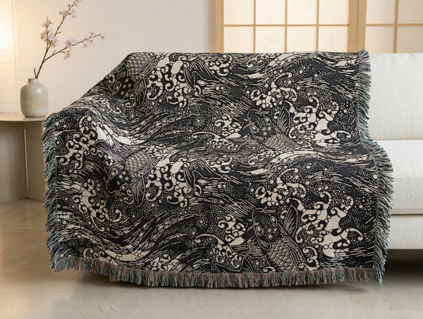 Decorative throw blanket with intricate dark blue and white pattern featuring koi fish, draped over a sofa.