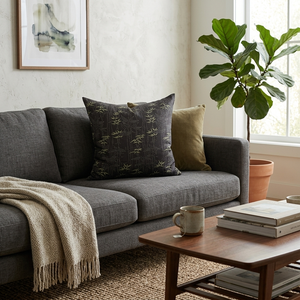 Cozy living room with a gray sofa, decorative pillows, a coffee table with books and a mug, and a plant.
