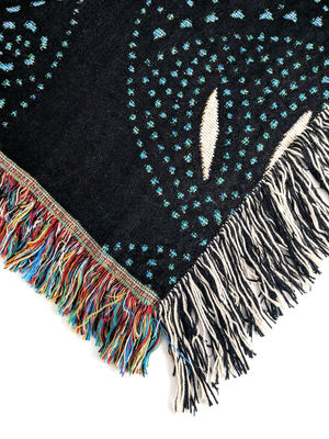 Corner edge of a woven blanket with a black background featuring a stylized pattern of scattered blue and green dots forming organic shapes.